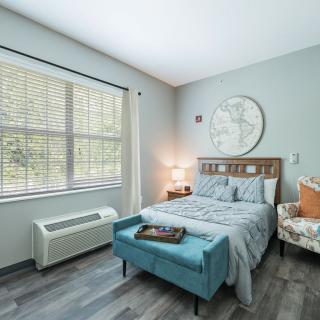 A modern bedroom with natural light, featuring a cozy bed, an armchair, and stylish decor.