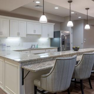 A modern kitchen featuring an island with granite countertops, white cabinets, and stylish pendant lighting.