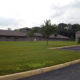 A view of a modern building surrounded by lush grass and trees under a cloudy sky.