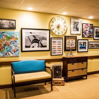 A cozy interior with a gallery wall displaying various artworks and a large clock, complemented by a wooden bench and cabinet.
