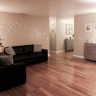 A modern living room with wood flooring, featuring a black sofa and decorative wall art.
