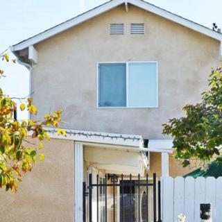 A two-story residential house with a gated entrance and surrounding trees.