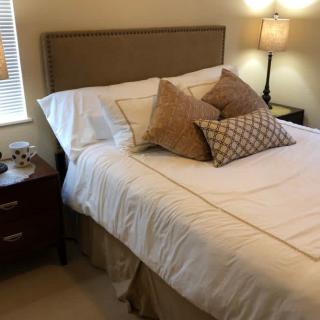 A cozy bedroom with a neatly made bed, adorned with multiple pillows and illuminated by a bedside lamp.