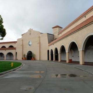 A building featuring a series of arches and a driveway, set against a cloudy sky.