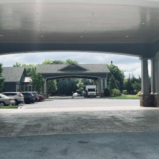 A view of a covered entryway with parked cars and greenery in the background.
