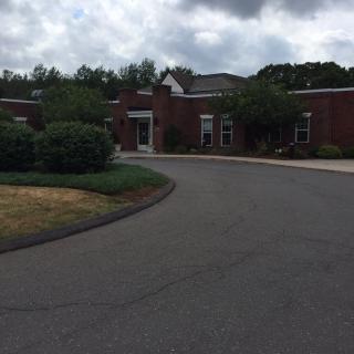 A brick building with a driveway and surrounding greenery under a cloudy sky.