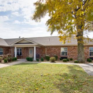 A brick residential house with a spacious lawn and a tree in the front yard.