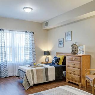 A cozy bedroom with two beds, a dresser, and soft natural lighting filtering through the window curtains.