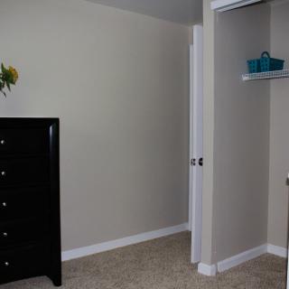 A minimalist bedroom featuring a dresser, an open closet, and neutral-colored walls.