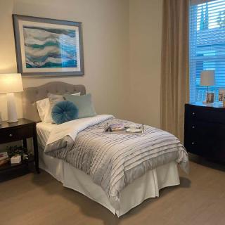 A cozy bedroom with a single bed, nightstand, and window, featuring a decorative painting above the headboard.