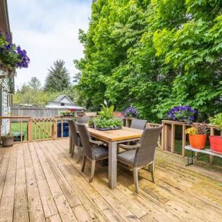 A wooden deck with outdoor furniture and colorful potted plants, surrounded by lush greenery.
