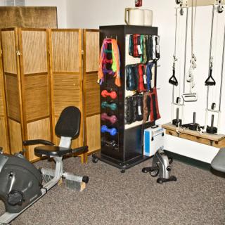 A well-equipped fitness room featuring various exercise equipment, including a rowing machine and a storage rack filled with colorful resistance bands.