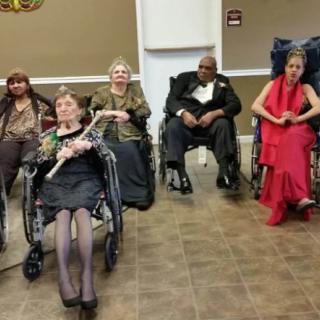 A group of people sitting indoors, some in wheelchairs, possibly attending an event.