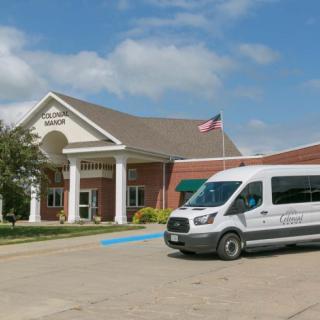 A van parked outside a brick building with a columned entrance under a cloudy sky.