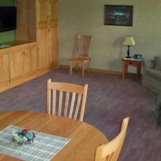 A cozy living room featuring a wooden dining table, chairs, a sofa, and entertainment center with a television.