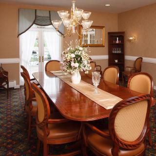 An elegant dining room with a long wooden table, upholstered chairs, and a decorative chandelier.