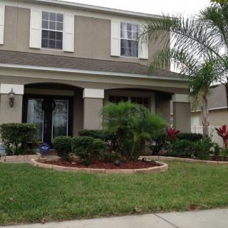 A suburban house with a well-maintained front yard featuring palm trees and shrubs.