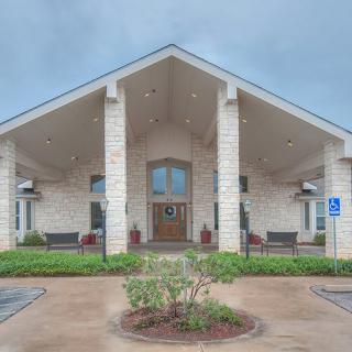 A symmetrical building entrance with columns, surrounded by landscaping under an overcast sky.