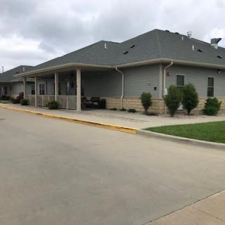 A residential building with a driveway and neatly trimmed shrubs under a cloudy sky.