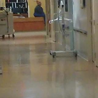A hospital hallway with medical equipment and a distant view of a person near the reception area.