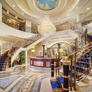 A luxurious hotel lobby with an ornate staircase and grand chandelier.