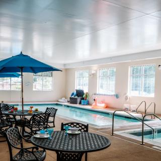 A cozy indoor pool area with tables, chairs, and a sun umbrella for relaxation.
