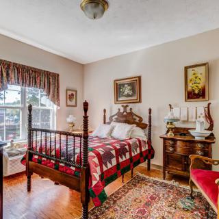 A cozy, traditional bedroom featuring a wooden bed with a colorful quilt and vintage decor.