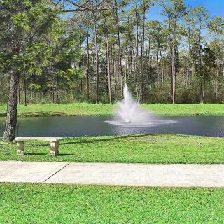 A serene park setting with a fountain in a pond, surrounded by trees and greenery.