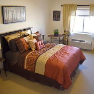 A cozy bedroom with a neatly made bed, decorative pillows, and warm lighting.