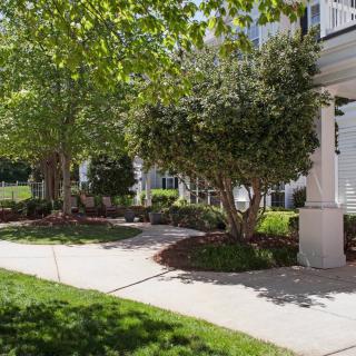 A tidy garden with trees and bushes lining a curved sidewalk in front of a house.