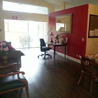 A cozy office space with a wooden floor, featuring a desk and chair against a red accent wall, and decor including a large mirror.