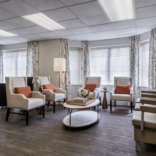 A modern living room with plush chairs, a round coffee table, and large windows with curtains.