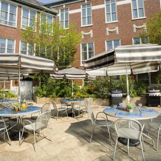 A cozy outdoor cafe patio with tables, chairs, and umbrellas surrounded by greenery.
