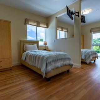 A cozy bedroom with two single beds, wooden flooring, and ample natural light through large windows.