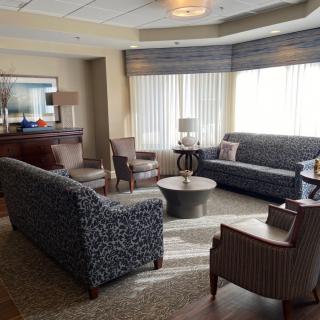A cozy living room with sofas and chairs arranged around a coffee table, featuring large windows for natural light.
