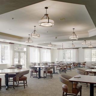 An empty dining area with neatly arranged tables and chairs under elegant lighting.