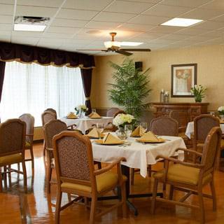 An elegantly set dining room with round tables, neatly arranged chairs, and warm decor.