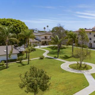 A scenic view of a landscaped garden with pathways, surrounded by buildings and lush greenery on a sunny day.