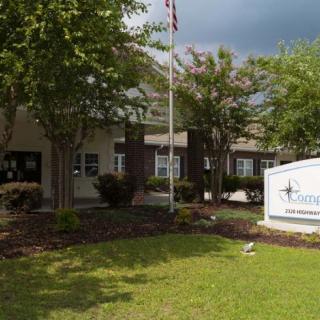A school building with a sign in the foreground surrounded by trees and a flagpole.
