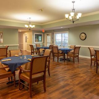 A cozy dining room with several tables and chairs arranged neatly, featuring warm lighting and wood flooring.