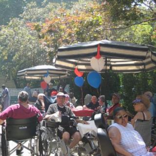 A group of people in wheelchairs enjoying an outdoor gathering under striped umbrellas decorated with balloons.