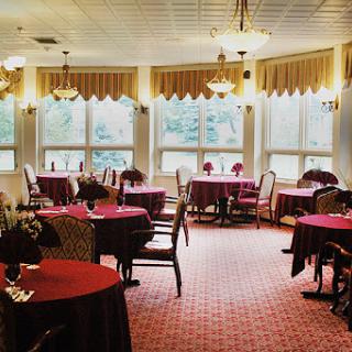 A cozy dining area featuring elegantly set tables with red tablecloths and ample natural light from large windows.