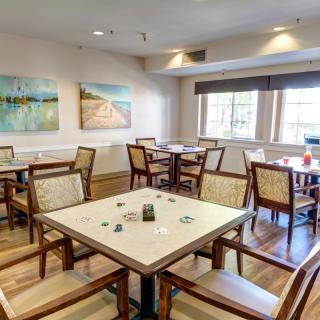 A cozy dining room featuring neatly arranged tables and chairs, with natural light streaming in through the windows and artwork adorning the walls.