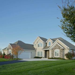 A suburban house with a well-maintained lawn and driveway under a clear blue sky.