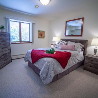 A cozy bedroom with a neatly made bed, bedside lamps, and a large window.