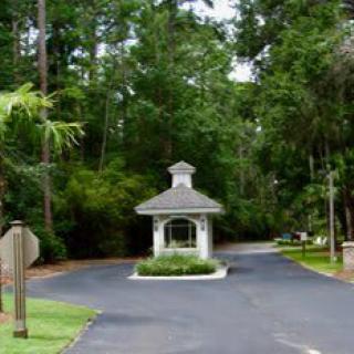 A small guardhouse situated at the entrance of a driveway surrounded by trees.