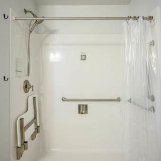 A modern, accessible white shower with grab bars and a shower curtain.