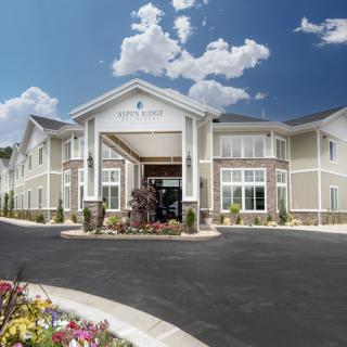 A modern building with a grand entrance, surrounded by landscaping and set against a blue sky with clouds.