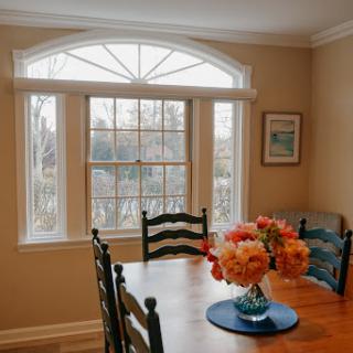 A cozy dining area featuring a wooden table adorned with a vibrant flower arrangement and large windows letting in natural light.