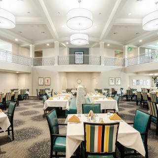 A spacious and elegantly designed dining room with neatly arranged tables and chairs, illuminated by large chandeliers.